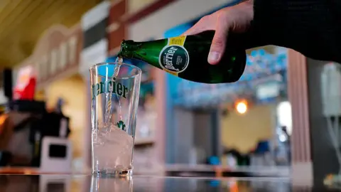 Getty Images A man pours a bottle of Perrier water into a glass on a bar