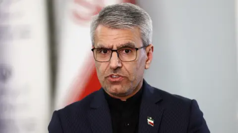 Reuters A man in black suit jacket speaks while looking into the camera