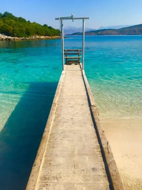 Amber Robertson A small pier on the beach in Albania. The water is a brilliant blue.