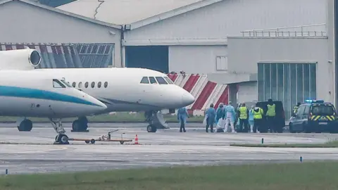 Reuters PPE-clad officials wait near a jet on the tarmac at an airport.