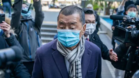 Getty Images Jimmy Lai wearing a blue mask walking among a crowd