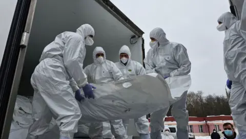 Medinski Instagram post Officials in white overalls that cover their heads and wearing face mask carry a white stretcher presumably containing a body being unloaded from what looks like a truck