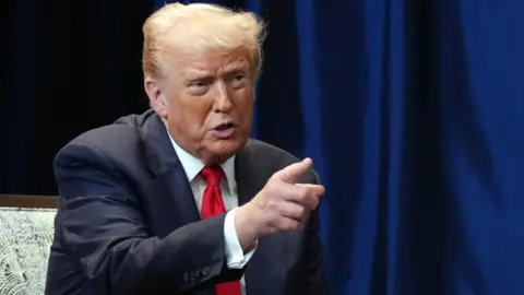 Getty Images Donald Trump points with his finger. He is wearing a navy suit, white shirt and red tie.