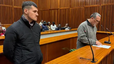 Nomsa Maseko/BBC Adrian de Wet, left, is seen wearing a black jacket while Zachariah Olivier is seen in a grey jacket in court