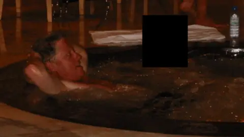 Reuters Bill Clinton reclines in a hot tub next to a person whose face has been covered by a black square to protect their identity