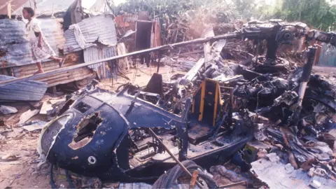 Scott Peterson / Getty Images The wreckage of a Black Hawk helicopter in Mogadishu in 1993. Behind it can be seem some houses made of corrugated iron sheets. A child is walking along one of the helicopter blades.