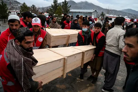AFP via Getty Images Afghan Red Crescent Society volunteers carry the coffins after offering funeral prayers for victims of a Pakistani air strike on a drug rehabilitation centre, during a mass burial ceremony at the Badam Bagh Hilltop in Kabul on March 18, 2026.