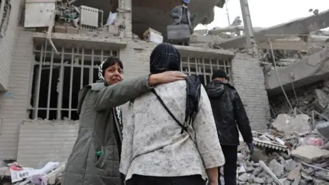 Reuters People gather next a damaged building in the aftermath of a strike, amid the U.S.-Israeli conflict with Iran, in Tehran, Iran, March 12, 2026