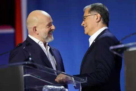 Los Angeles Times via Getty Images Both candidates appear on stage near a podium. They are shaking hands and smiling. 