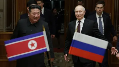 Getty Images Kim Jong Un (left) smiles as he walks alongside Vladimir Putin (right) in front of the national flags of North Korea and Russia