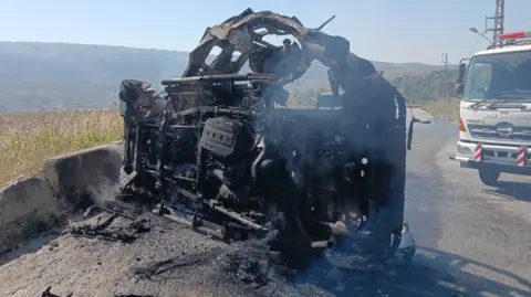 Lebanese Army The burnt out remains of a car lying on a road in Lebanon, with a recovery vehicle nearby 