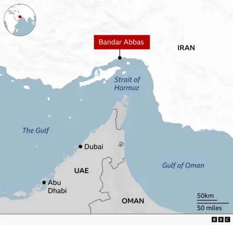 A BBC map of the Strait of Hormuz region, showing the narrow strait between The Gulf to the west and the Gulf of Oman to the east. The north of the strait is the coast of Iran and the United Arab Emirates and Oman are to the south. Bandar Abbas is highlighted in red on the Iranian coast at the narrowest point of the strait. The map also labels Dubai and Abu Dhabi in the UAE on The Gulf coast. A small inset map shows the location of the region within the Middle East and between Africa and Asia.