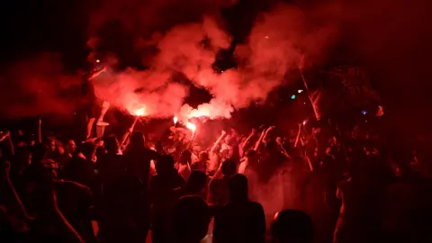 Anadolu via Getty Images PSG supporters release flares during clashes with police in Paris.
