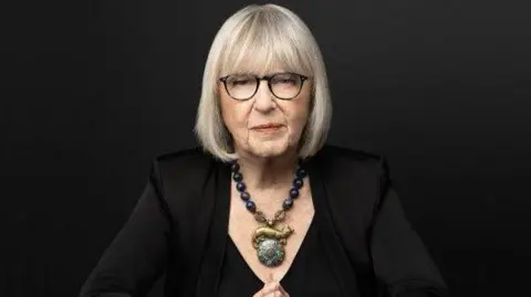 Beowulf Sheehan A professional headshot of Harriet Newman Cohen, where she wears a black top, large statement necklace. Her hair is cut in a silver bob