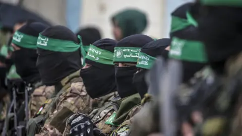 EPA-EFE/REX/Shutterstock Armed fighters from Hamas' Izz ad-Din al-Qassam Brigades stand guard during the handover of three Israeli hostages to Red Cross representatives in Al Nuseirat refugee camp, central Gaza Strip,