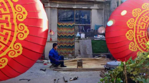 A Man sits on a stoll while working on red Lunar New Year lanterns in China