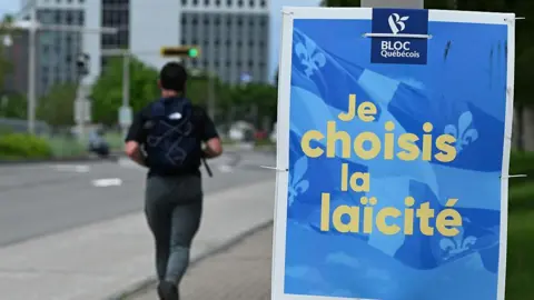 NurPhoto via Getty Images A man jogs by a blue and yellow political campaign poster that reads in French 'I choose secularism' is seen in Longueuil, 