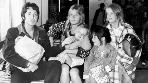 Daily Express/Getty Images Paul McCartney poses with his wife Linda (1941 - 1998), and their daughters, left to right, Stella, Mary, and Heather, at Heathrow Airport in London, England, 2nd August 1974