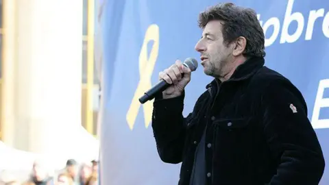 AFP via Getty Images French singer and actor Patrick Bruel speaks through a microphone during a rally in 2025