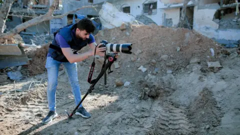 Missing journalist Haitham al-Wahad taking a photo against a backdrop of heaped soil and rubble