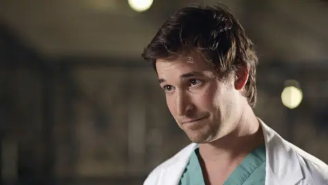 Getty Images Noah Wyle as Doctor John Carter in TV show ER. He's pictured in scrubs, looking away from the camera. 