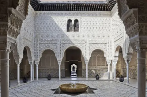 US Department of Justice A courtyard with tiled floor, fountain and white ornately carved walls 
