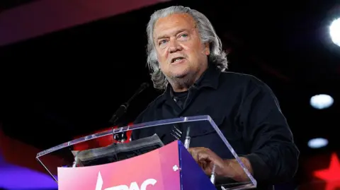 Bloomberg via Getty Images Steve Bannon speaks at the Conservative Political Action Conference (CPAC). He wears a black shirt and stands at a glass podium.