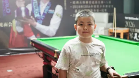 A small boy stands beside a snooker table