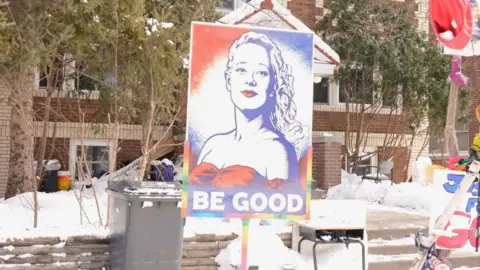 BBC / Brian Khisa A poster image showing Renee Good with the slogan 'Be Good' in tribute to her seen on a snowy street in Minnesota 