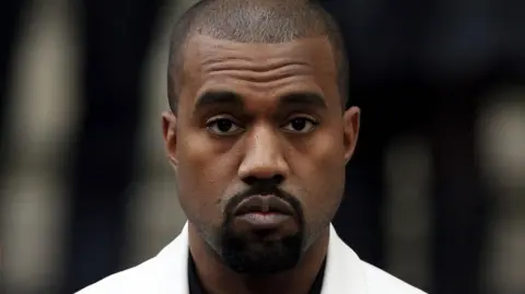 PA Media Kanye West in a white suit looking at the camera in 2015