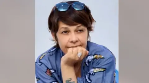 unicef Karine Buisset, who has her hand on her mouth. She is wearing a blue top and has medium-length brown hair with sunglasses on her head.