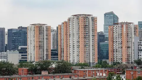 Getty Images Several orange and white high-rise apartment buildings stand in front of modern high-rise buildings in Beijing
