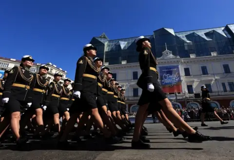 Reuters Russian service members march in rows along a road in Vladivostok. The regiment is made up of women wearing black and gold uniforms.