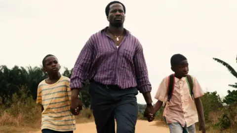 MUBI An actor is walking, holding the hands of two children, in the film