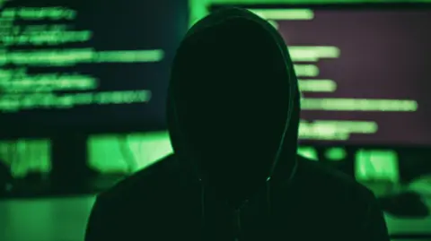 Getty Images Anonymous internet hacker in front of computer monitors. Obscured face.