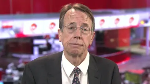 BBC Biobank chief executive Professor Sir Rory Collins, wearing a grey suit, white shirt and paisley tie, looks at the camera as he speaks to BBC Breakfast. The BBC News newsroom in London is in the background behind him. 