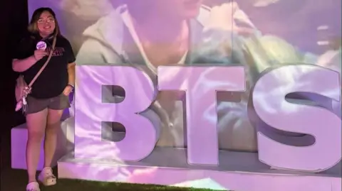 Supplied Cookie poses beside a purple BTS signage at an event organised by Army