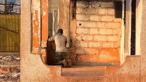 Reuters A man sits on his knees in a brick building looking through a window