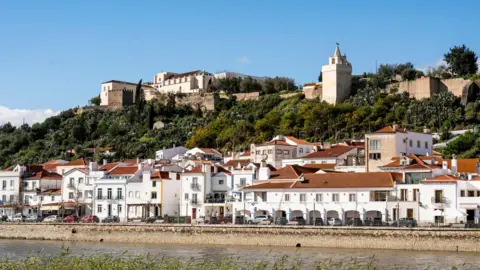 Getty Images A row of houses by a river, with green trees above 