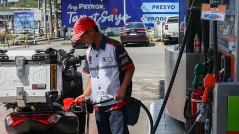 Getty Images A man fills up a motorbike engine with fuel as vehicles wait in queue at a petrol station 