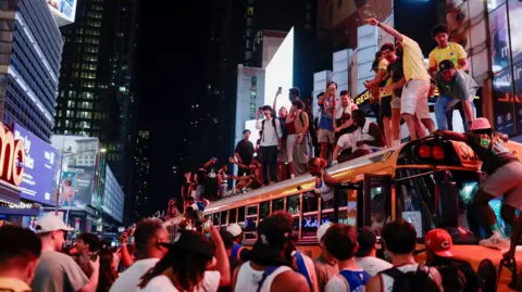 REUTERS/Jeenah Moon People stand on a yellow school bus celebrating at night in Times Square in New York