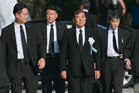 Getty Images Ishiba wearing a black suit walking. He is flanked by other men in black suits.