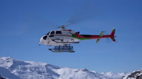 BBC A helicopter is seen over snowy mountains
