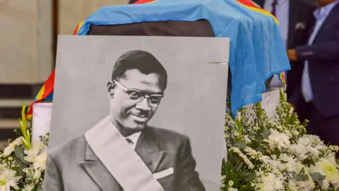 AFP via Getty Images A portrait of assassinated Congolese independence hero Patrice Lumumba is seen near the casket containing his only surviving remains at Palais du Peuple in Kinshasa on 27 June 2022. 