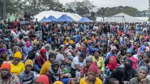 AFP via Getty Images A big crowd of migrants sitting in an open space in Durban