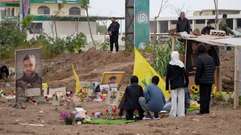 Neha Sharma/BBC Lebanese gather next to graves at a cemetery in southern Lebanon, where Hezbollah flags and photos of Hezbollah fighters are on display