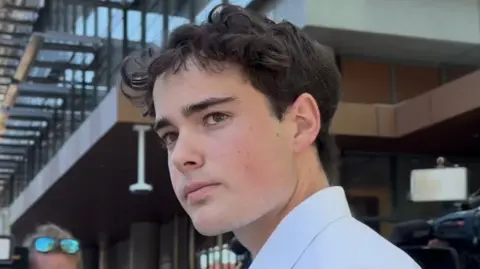 Australian Broadcasting Corporation/Eva Blandis A young man with brown hair and a white shirt looks at the camera