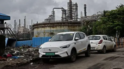NurPhoto via Getty Images An electric car is parked near an oil refinery in Mumbai, India. 
