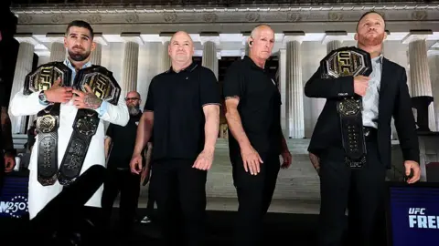 Zuffa LLC via Getty Images Two fighters holding UFC belts standing beside others in front of the Lincoln Memorial