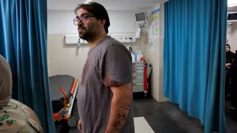 Reuters A Palestinian father stands in a Hebron hospital emergency room with his clothes stained with blood. His his seven-month-old baby was killed by Israeli forces, the Palestinian health ministry said. Photo: 5 June 2026